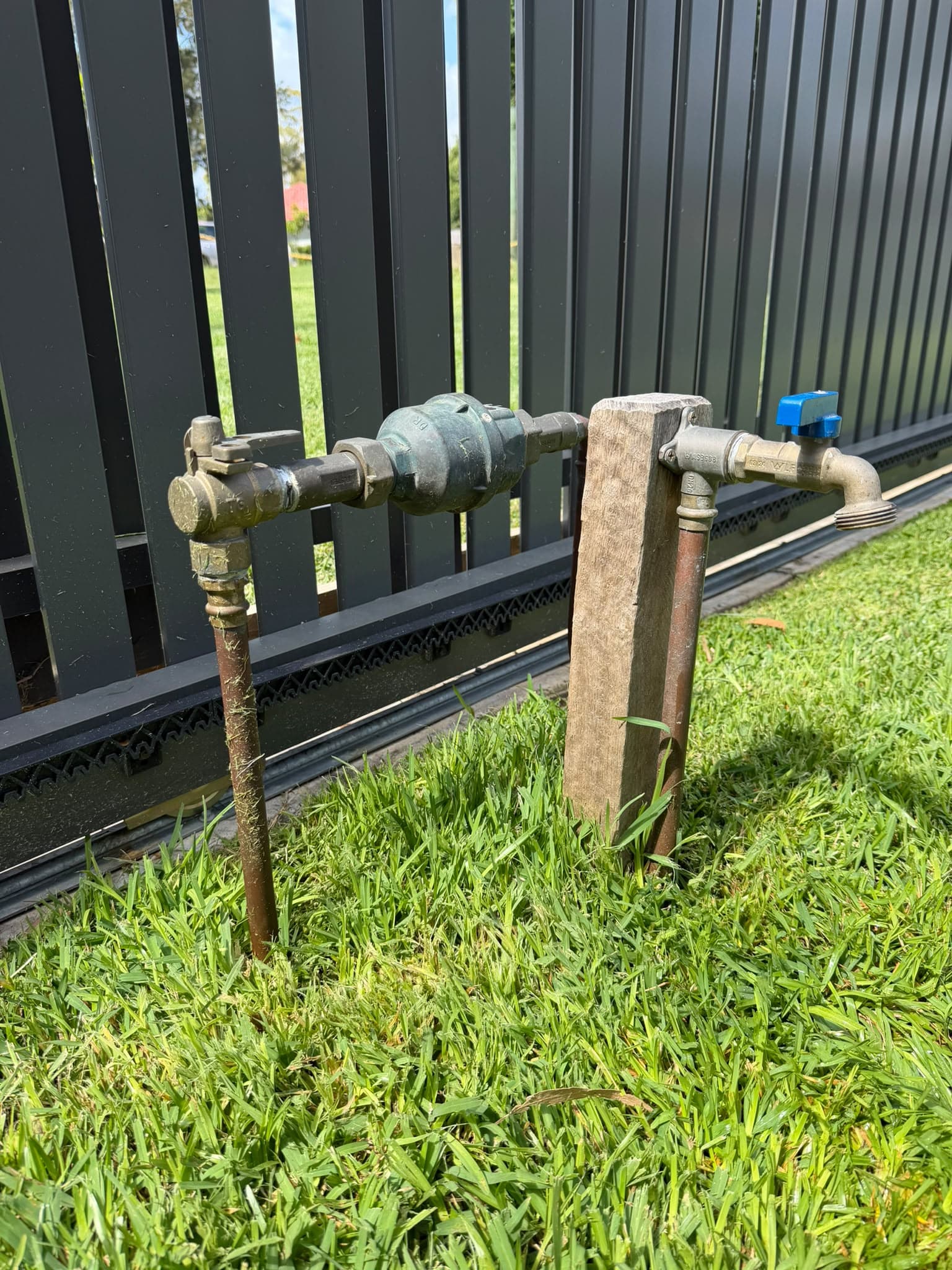 Outdoor tap, water meter and copper connections beside a fence