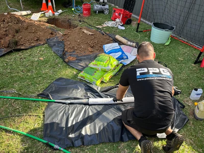 Panther plumber in branded workwear beside an excavated drain