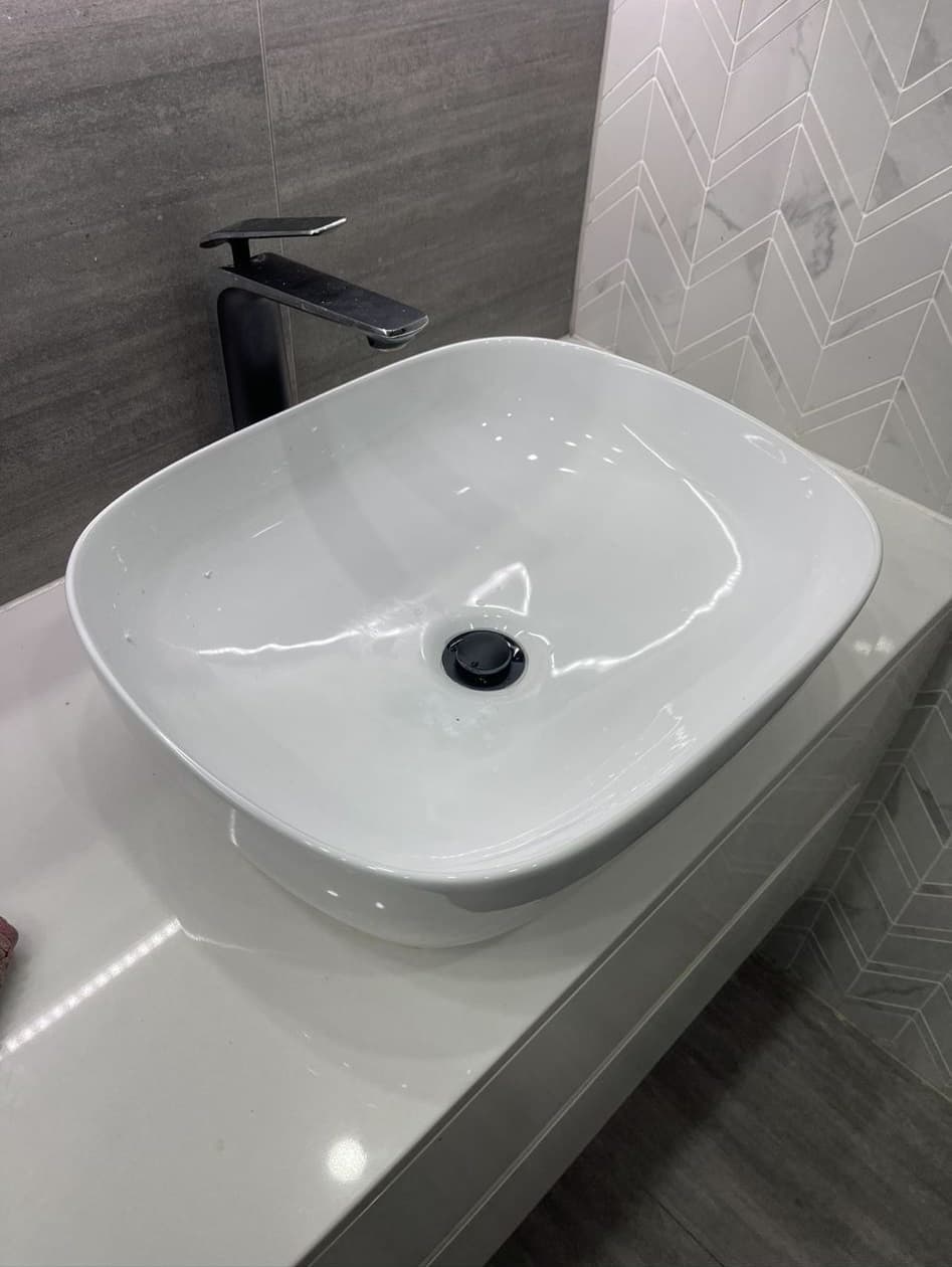 White countertop basin with a black mixer and waste fitting