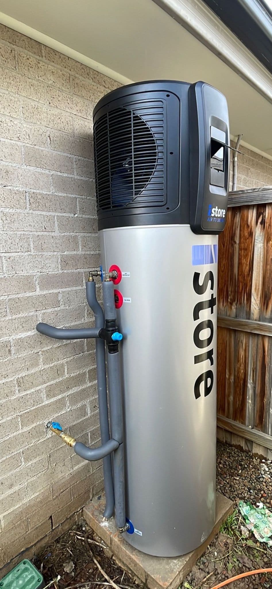 Heat-pump water heater beside a wall and timber fence