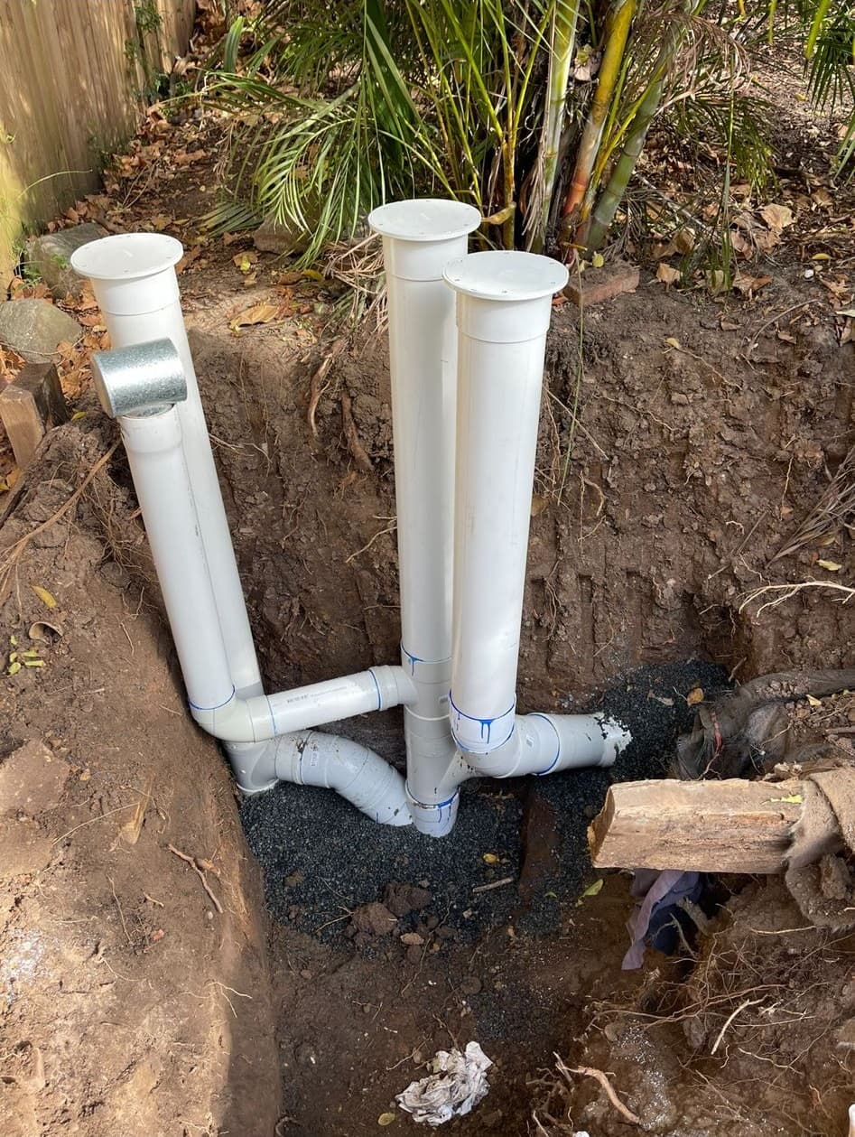 Exposed drain junctions and upright access pipes in an excavation