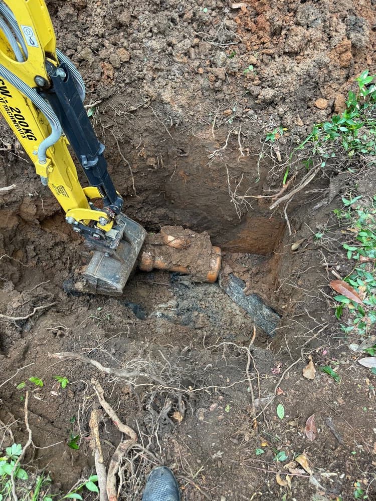 Excavator bucket beside an exposed underground pipe