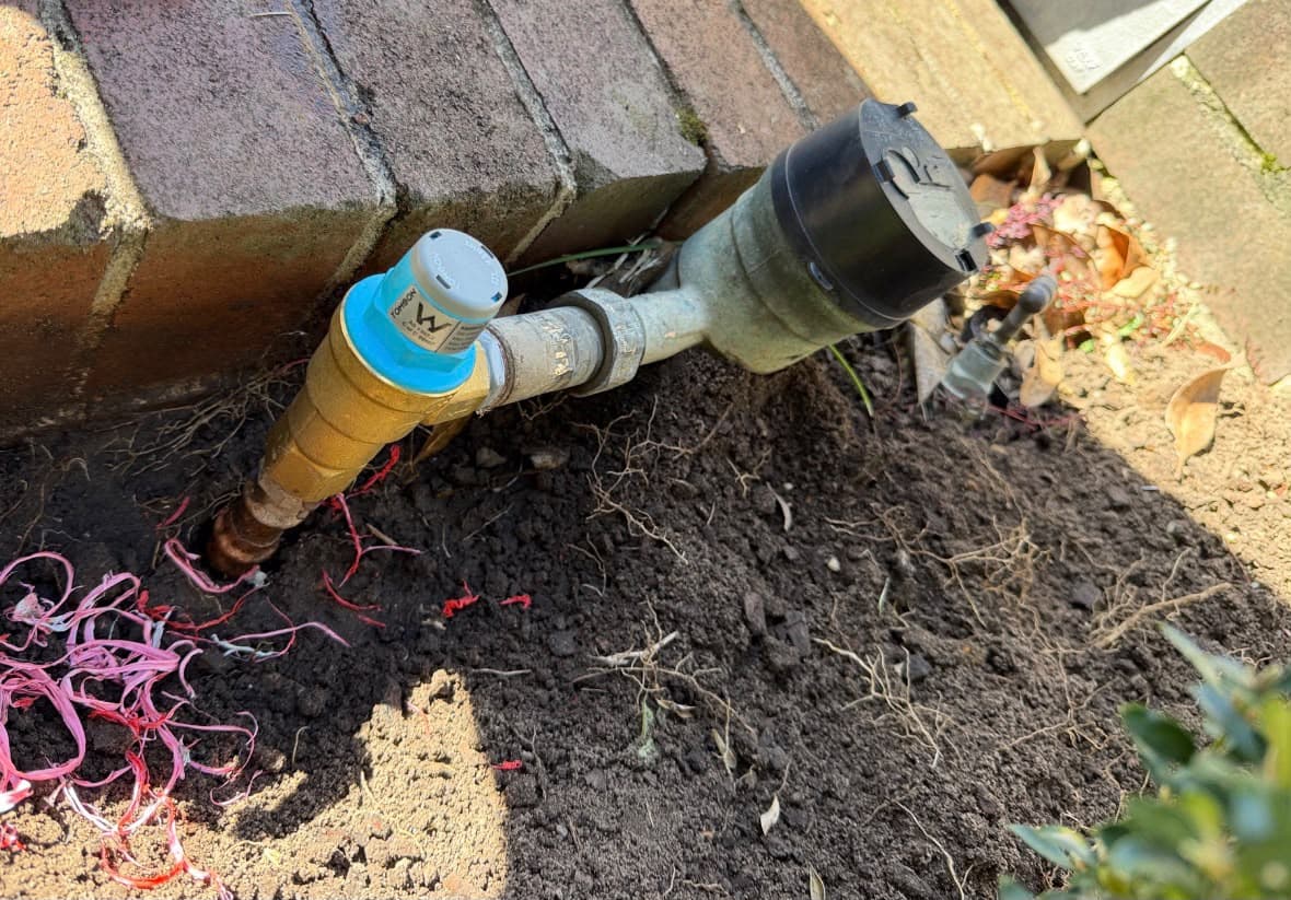 Water meter, brass valve and copper connection beside a brick wall